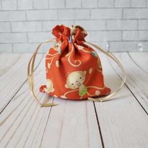 May include: A small orange drawstring bag with a monkey print. The bag has gold drawstrings.