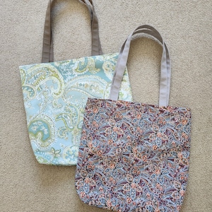 May include: Two tote bags with paisley patterns. One bag is light blue with green and yellow paisley, the other is dark blue with red, orange, and white paisley.