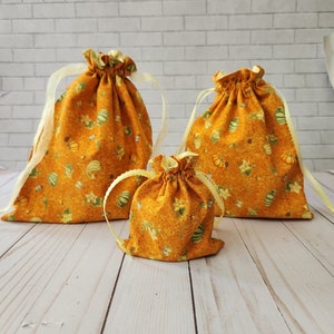 May include: Three orange fabric drawstring bags with a pumpkin and floral print. The bags are different sizes and are arranged on a light wood surface.