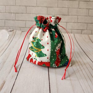 May include: A small red and green drawstring bag with a Christmas tree and stocking pattern. The bag is made of fabric and has a white background.