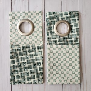 May include: Two green and white fabric panels with grommets. The panels have a checkered pattern with a smaller green design.