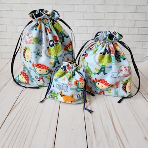 May include: Three blue drawstring bags with a pirate and animal print design. The bags are different sizes and have black drawstrings.