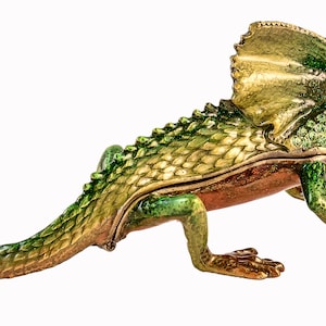 May include: A green and gold jeweled lizard trinket box with a frilled neck and a long tail.