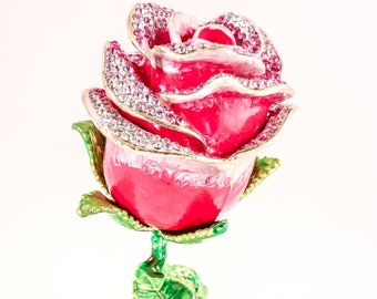 May include: A decorative rose figurine with a vibrant red bloom, accented with sparkling rhinestones around the petals. The stem and leaves are painted green with gold accents, creating a striking contrast against the white background.