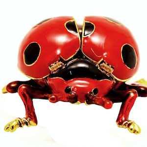 May include: A red and black ladybug trinket box with gold accents. The box is open and the wings are raised.