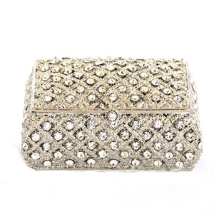May include: A silver jewelry box with a diamond-like pattern and clear rhinestones.