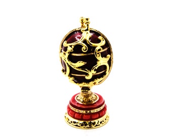 May include: A red and gold decorative egg with intricate gold filigree designs. The egg is on a red and gold stand.