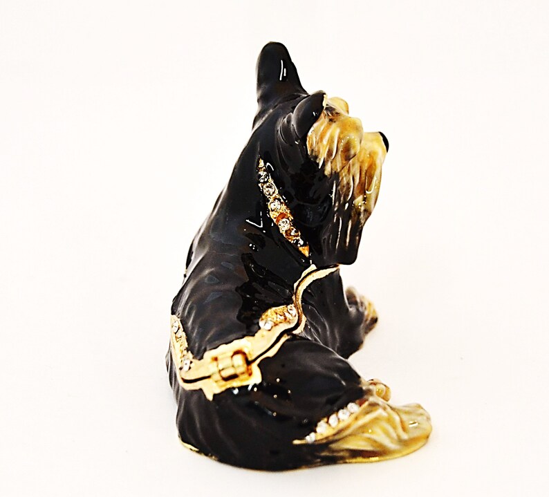 Puede incluir: Figura de metal negro y dorado de un perro sentado con pedrer&iacute;a. El perro tiene una cola larga y esponjosa y mira hacia la derecha.