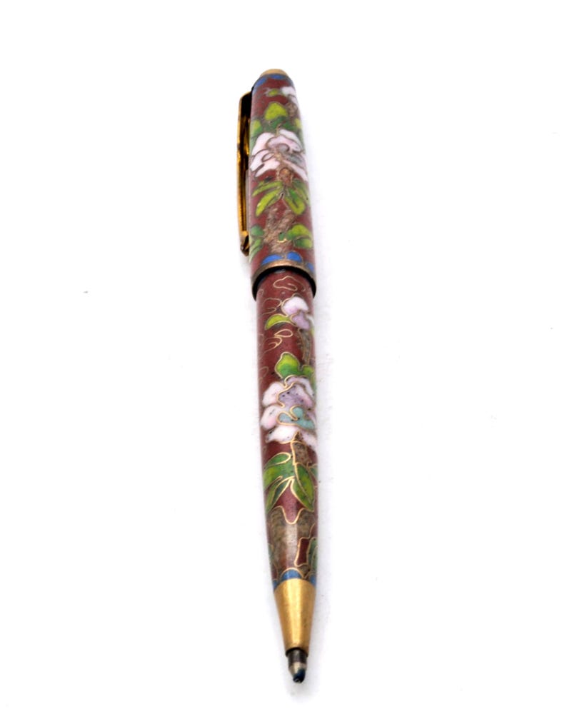 Puede incluir: Un bol&iacute;grafo decorativo con un cuerpo granate, adornado con motivos florales blancos y morados y hojas verdes. El bol&iacute;grafo presenta un clip y una punta dorados, y un acento azul cerca de la punta. Es un instrumento de escritura.