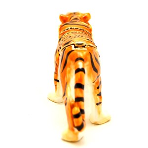 May include: A ceramic tiger figurine with orange and black stripes. The figurine is standing on a white surface and is facing away from the camera.
