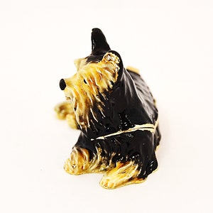 Puede incluir: Una figurita de Yorkshire Terrier negra y marr&oacute;n con detalles dorados. La figurita est&aacute; sentada con la cabeza girada hacia un lado. Est&aacute; hecha de metal y tiene un dise&ntilde;o detallado.