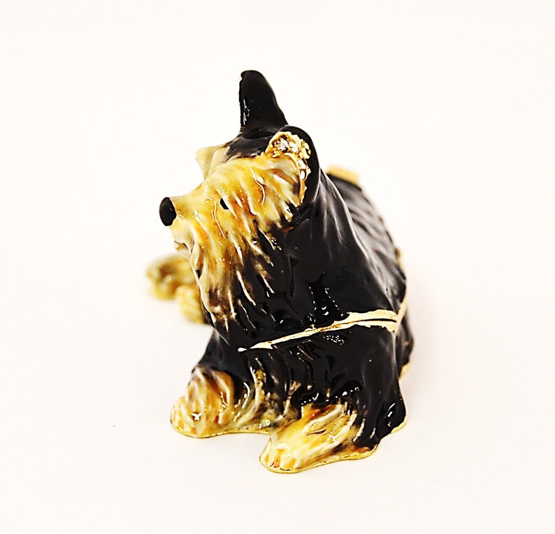 Puede incluir: Una figurita de Yorkshire Terrier negra y marr&oacute;n con detalles dorados. La figurita est&aacute; sentada con la cabeza girada hacia un lado. Est&aacute; hecha de metal y tiene un dise&ntilde;o detallado.