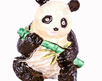 Puede incluir: Una figurita de panda blanco y negro sosteniendo un tallo de bambú verde. La figurita está hecha de metal y tiene un acabado brillante.