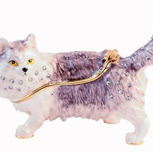 May include: A white and gray cat figurine with a gold hinge and rhinestones. The cat is standing with its tail raised.