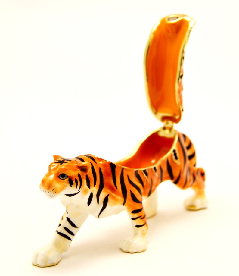 May include: A small, orange and black tiger figurine with a hinged back that opens to reveal a small compartment. The figurine is made of porcelain and has a glossy finish.