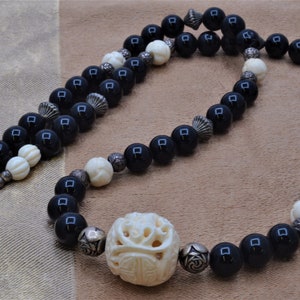 May include: A black and white beaded necklace with a large carved bone bead. The necklace has a silver clasp and is made with black onyx and white bone beads.