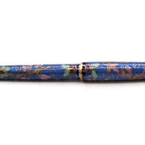 Puede incluir: Un bol&iacute;grafo azul con un dise&ntilde;o floral. El bol&iacute;grafo tiene una punta y detalles dorados. El patr&oacute;n floral incluye detalles rosas, verdes y dorados. El bol&iacute;grafo es un instrumento de escritura.