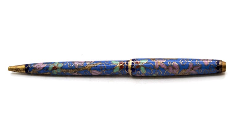 Puede incluir: Un bol&iacute;grafo azul con un dise&ntilde;o floral. El bol&iacute;grafo tiene una punta y detalles dorados. El patr&oacute;n floral incluye detalles rosas, verdes y dorados. El bol&iacute;grafo es un instrumento de escritura.