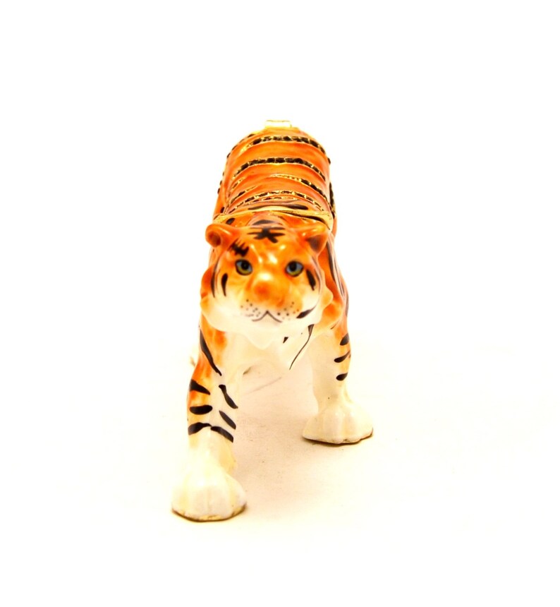 May include: A ceramic tiger figurine with orange and black stripes. The tiger has a white face with black eyes and a pink nose.