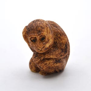 May include: A small, intricately carved wooden monkey figurine. The monkey is brown and has a distressed finish. It is sitting with its head down and its hands covering its ears.