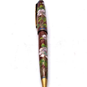Puede incluir: Un bol&iacute;grafo decorativo con un dise&ntilde;o floral. El bol&iacute;grafo presenta un color base rojo oscuro con patrones florales blancos, verdes y azules. El bol&iacute;grafo tiene un clip y una punta dorados.