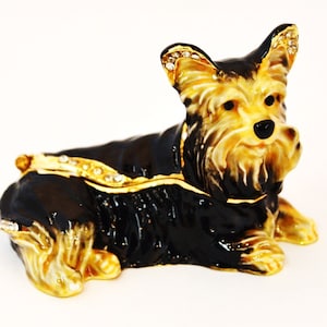Puede incluir: Una figurita de metal negro y dorado de un Yorkshire Terrier con pedrer&iacute;a. El perro est&aacute; tumbado con la cabeza girada hacia un lado. La figurita es una caja de recuerdos.