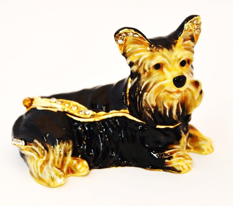 Puede incluir: Una figurita de metal negro y dorado de un Yorkshire Terrier con pedrer&iacute;a. El perro est&aacute; tumbado con la cabeza girada hacia un lado. La figurita es una caja de recuerdos.