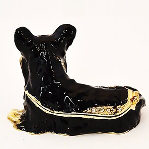 Puede incluir: Caja de metal negra con forma de perro. La caja tiene una tapa con bisagras y est&aacute; decorada con ribetes dorados y diamantes de imitaci&oacute;n.