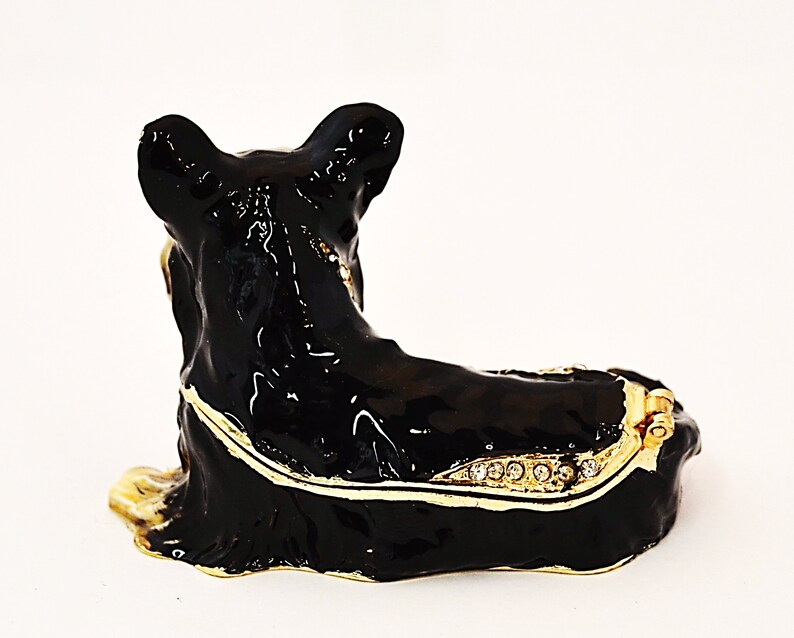 Puede incluir: Caja de metal negra con forma de perro. La caja tiene una tapa con bisagras y est&aacute; decorada con ribetes dorados y diamantes de imitaci&oacute;n.