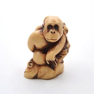 May include: A small, carved ivory sculpture of a monkey holding a smaller monkey. The sculpture is detailed and realistic, with the monkeys' features clearly defined.