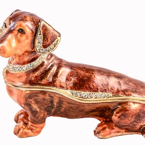 May include: A brown dachshund figurine with gold accents and rhinestones. The figurine is a decorative trinket box.