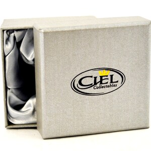 Puede incluir: Una caja de regalo gris con un interior de sat&eacute;n. La caja tiene un logotipo negro y dorado que dice "CIEL Collectables".