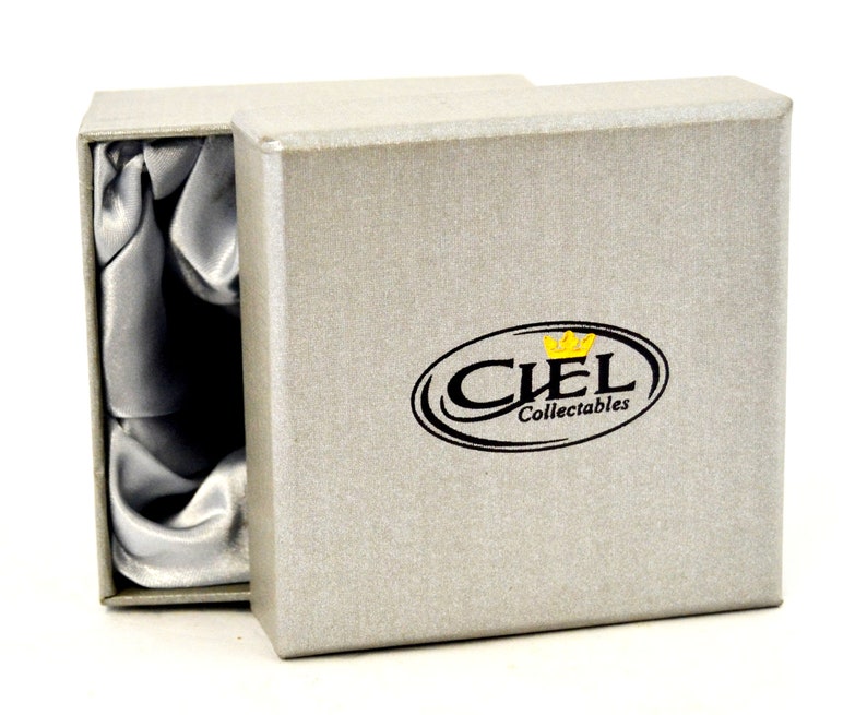 Puede incluir: Una caja de regalo gris con un interior de sat&eacute;n. La caja tiene un logotipo negro y dorado que dice "CIEL Collectables".