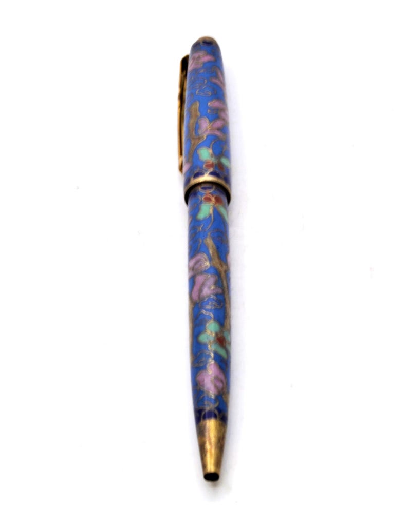 Puede incluir: Un bol&iacute;grafo azul con un dise&ntilde;o floral. El bol&iacute;grafo presenta un clip y una punta dorados, y el cuerpo est&aacute; adornado con un patr&oacute;n de flores y hojas rosas, verdes y doradas. El bol&iacute;grafo est&aacute; sobre un fondo blanco.