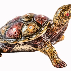Peut inclure: Une figurine de tortue décorative avec une carapace détaillée présentant un motif multicolore avec des accents dorés et des strass. La tortue est en métal et a une apparence réaliste.