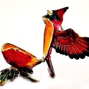 May include: A red cardinal bird trinket box with gold accents and a hinged lid. The box is open and the bird's wings are spread out.