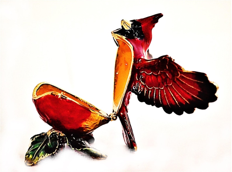 May include: A red cardinal bird trinket box with gold accents and a hinged lid. The box is open and the bird's wings are spread out.