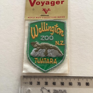 May include: A green and gold embroidered patch from the Wellington Zoo in New Zealand, featuring a tuatara reptile. The patch is part of the "World Wide Collectors Series" by Voyager.