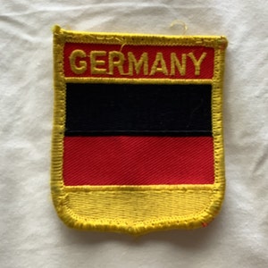 May include: A yellow, black, and red embroidered patch with the word "GERMANY" in yellow lettering.