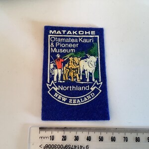 May include: A blue rectangular patch with the text "MATAKOHE Otamatea Kauri & Pioneer Museum Northland NEW ZEALAND". The patch features a graphic of a person, three animals, and trees.