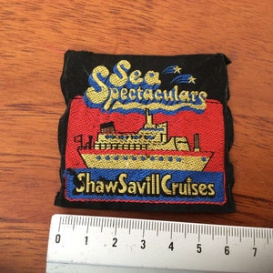 Könnte beinhalten: Ein schwarzer Stoff-Patch mit einem gestickten Design in Rot, Blau und Gelb. Das Design zeigt ein Schiff mit dem Text "Sea Spectaculars Shaw Savill Cruises".