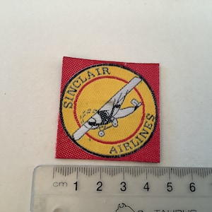 May include: A red fabric patch with a yellow circle containing a black and white airplane and the text "SINCLAIR AIRLINES".
