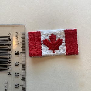 May include: Embroidered Canadian flag patch. The rectangular patch features a white center with a red maple leaf and red vertical bars on each side. The patch is approximately 1.5 inches wide and 1 inch tall.
