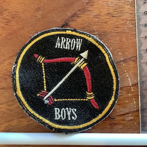 Könnte beinhalten: Ein gestickter schwarzer und gelber Aufnäher mit einem roten und weißen Pfeil und dem Text "ARROW BOYS".