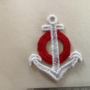 Könnte beinhalten: Weiß gestickter Anker mit einem roten Kreis in der Mitte. Der Anker ist ein beliebtes nautisches Symbol.