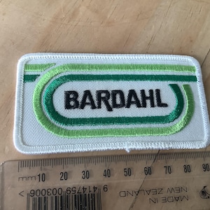 May include: Embroidered patch with the word "BARDAHL" in black, framed by green and white stitching. The patch is rectangular with rounded corners. A ruler is placed below the patch, showing measurements in millimeters.