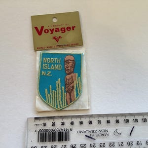 May include: A blue and yellow embroidered patch with the text "North Island N.Z." and a cartoon image of a person. The patch is a product of Voyager, a World Wide Collectors Series.