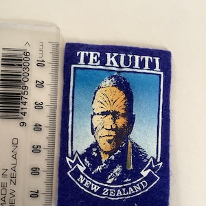 May include: A rectangular blue patch with the text "TE KUITI" at the top and "NEW ZEALAND" at the bottom. The patch features a portrait of a person with facial markings, set against a blue and white background.