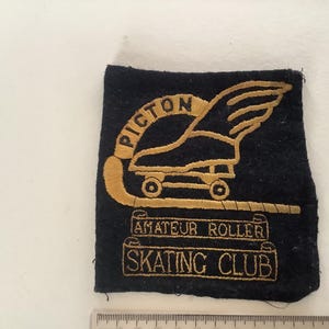 Pode incluir: Patch bordado vintage com um desenho de patins e as palavras "PICTON AMATEUR ROLLER SKATING CLUB" em fio dourado sobre fundo azul marinho. O patch tem formato retangular.