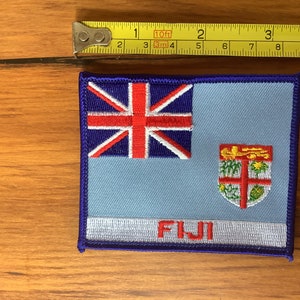 May include: A blue and white embroidered patch with the Fijian flag and the word "FIJI" in red lettering.